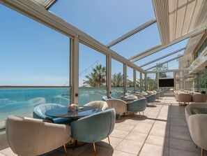 Un espace extérieur lumineux, aménagé pour accueillir les clients, avec vue sur l’océan, comprenant des tables rondes et des chaises modernes.