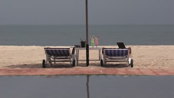 A beachside pool area with two lounge chairs and a table under a large umbrella.