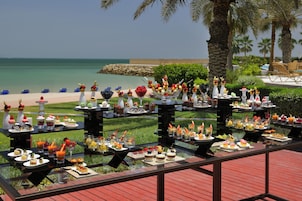A buffet table with various dishes and drinks, set against a backdrop of a beach and palm trees.