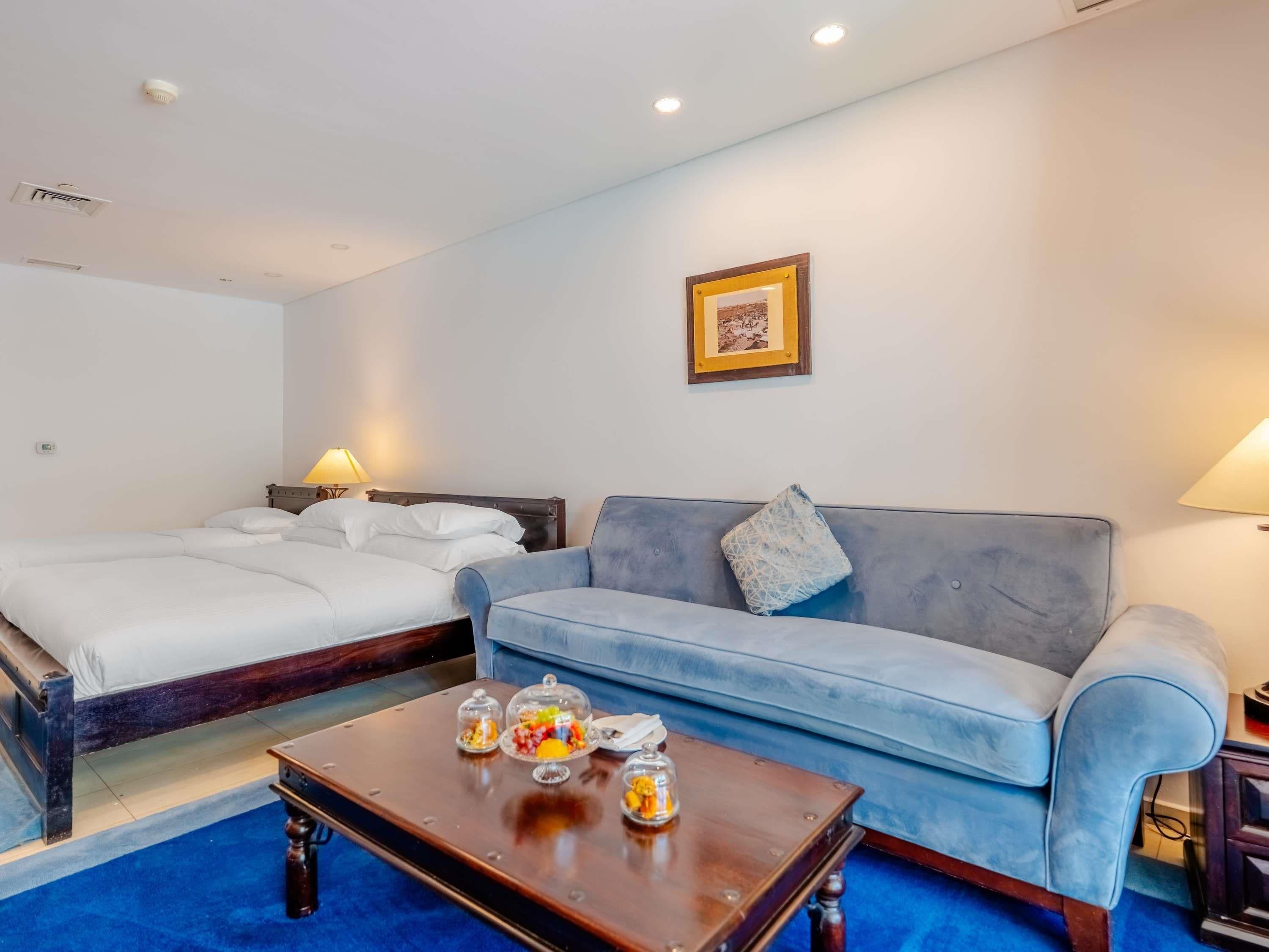 Een hotelkamer met een bed, een bank, een bijzettafeltje met decoratieve objecten en een ingelijste foto aan de muur.