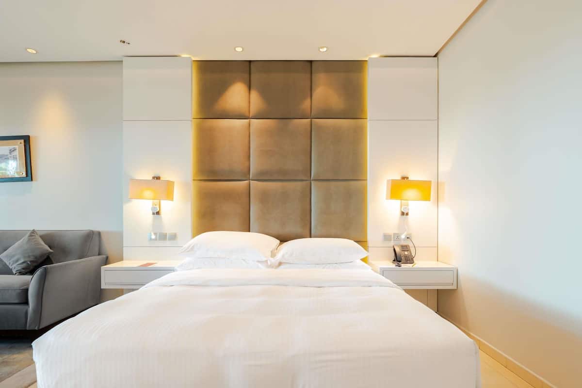 Ein Hotelzimmer mit einem großen Bett, zwei Nachttischen, einem Schlafsofa und einem an der Wand befestigten Kopfteil.