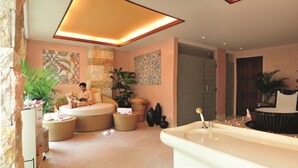 Une salle de bain moderne avec une grande baignoire, un coin salon où une personne est assise en train de lire, et des œuvres d’art décoratives au mur.