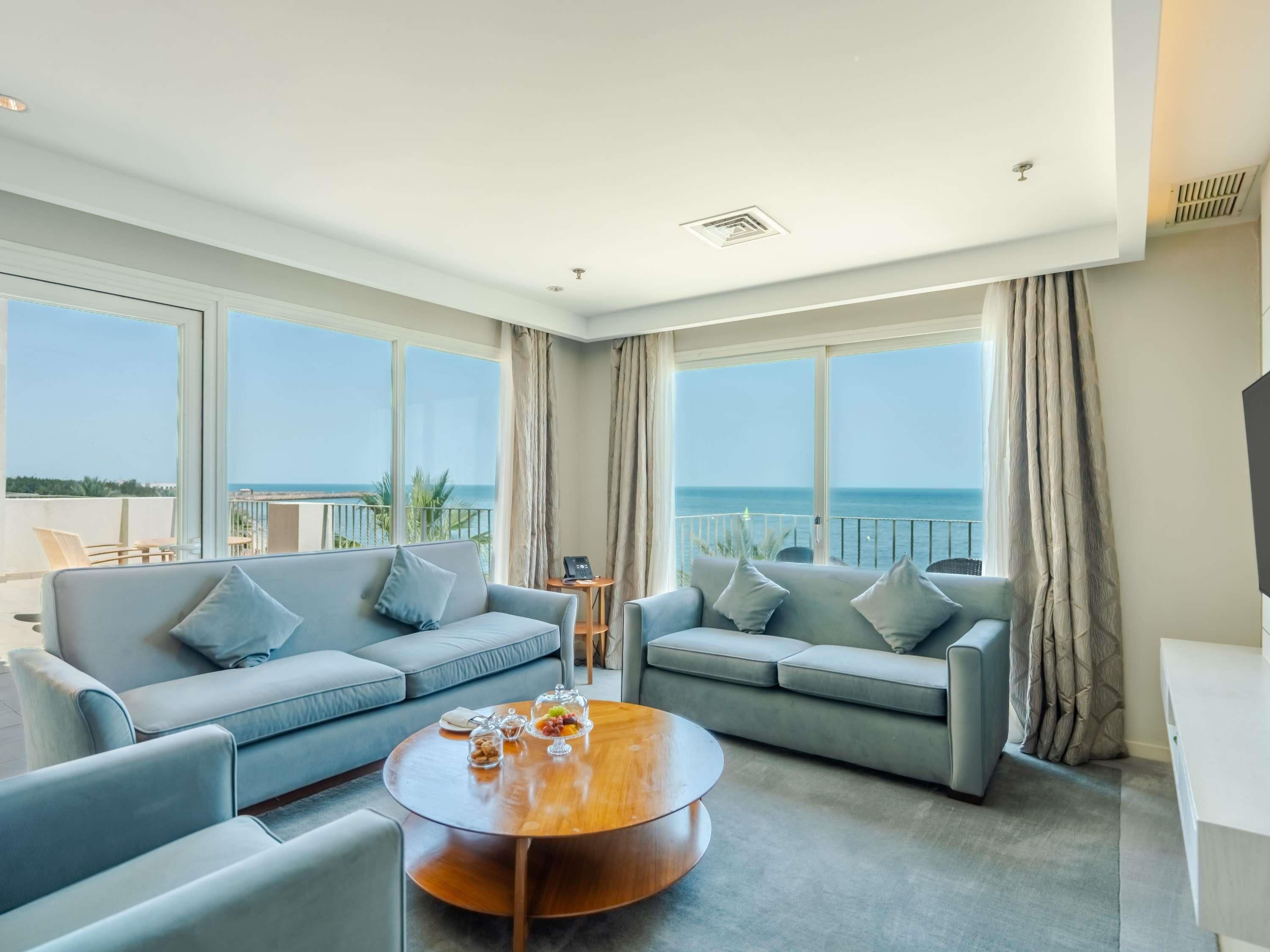 A modern living room with two sofas, a coffee table, and large windows offering a view of the sea.