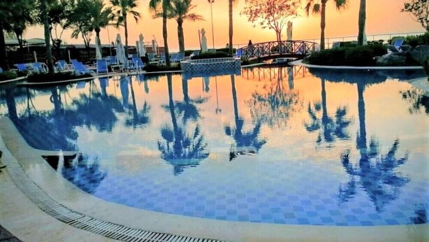 Una piscina con palmeras y una puesta de sol al fondo.