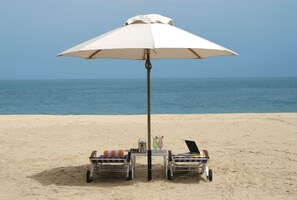Eine Strandkulisse mit einem weißen Sonnenschirm, zwei Liegestühlen, einem Tisch mit Getränken und einem Laptop.