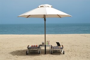 A beachside setting with a white umbrella, two lounge chairs, a table with drinks, and a laptop.