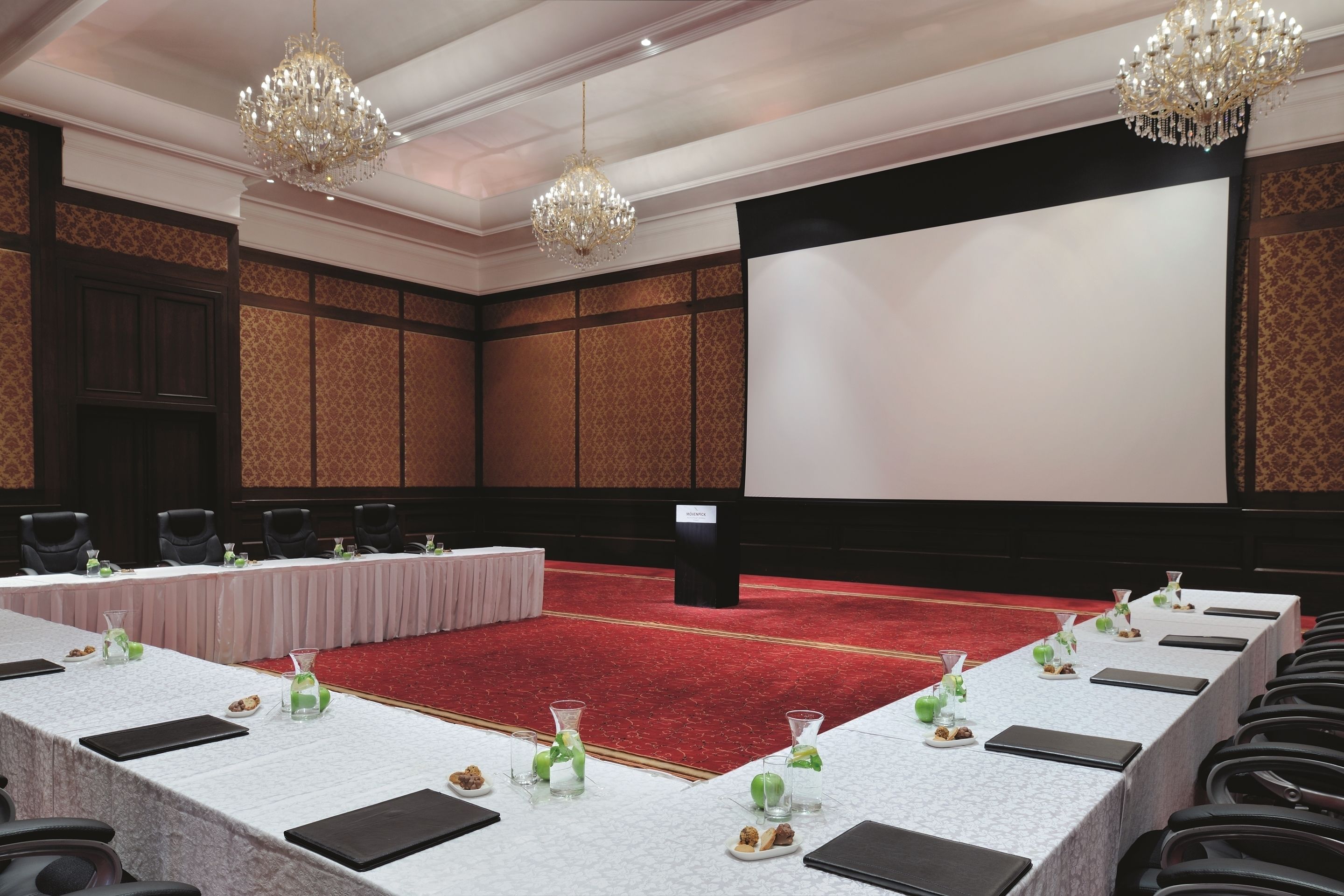 A conference room with a long table set for a meeting, a red carpet, and two chandeliers.