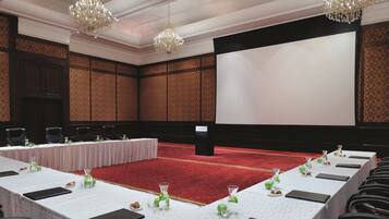 A conference room with a long table set for a meeting, a red carpet, and two chandeliers.