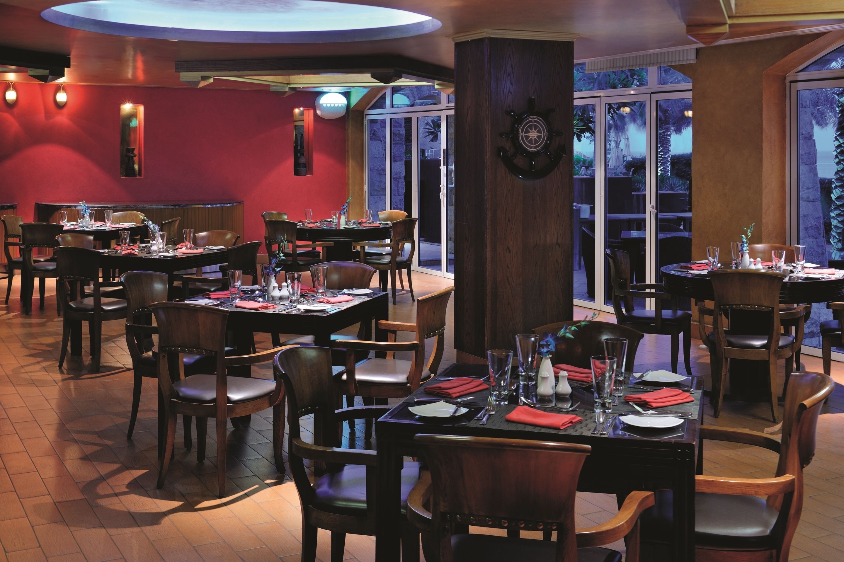 Ein Restaurant mit mehreren Tischen und Stühlen, großen Fenstern und einer Wanddekoration im Seestil.
