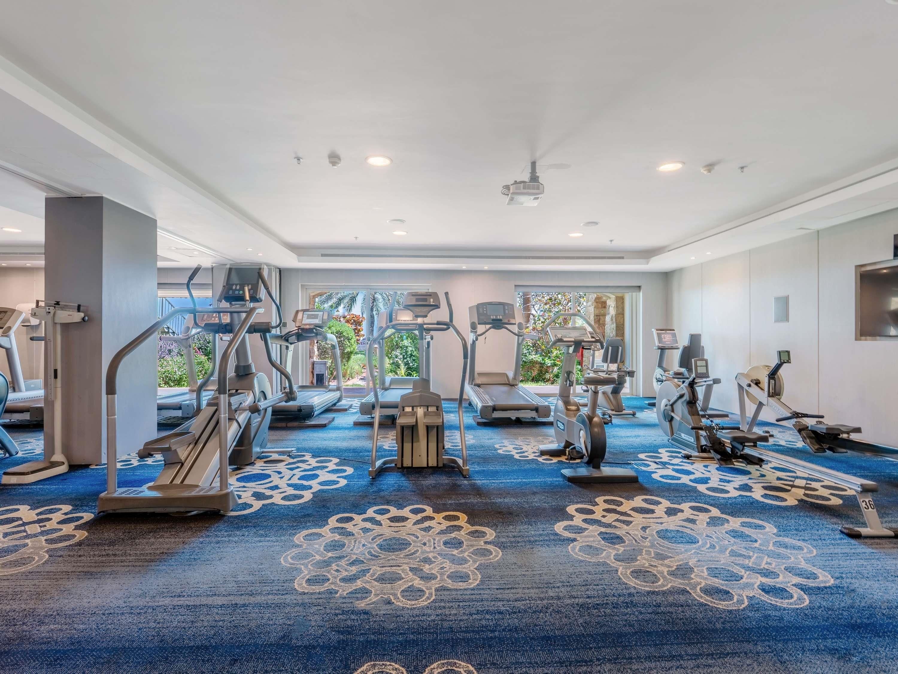 A hotel gym with treadmills, ellipticals, and a ceiling fan.