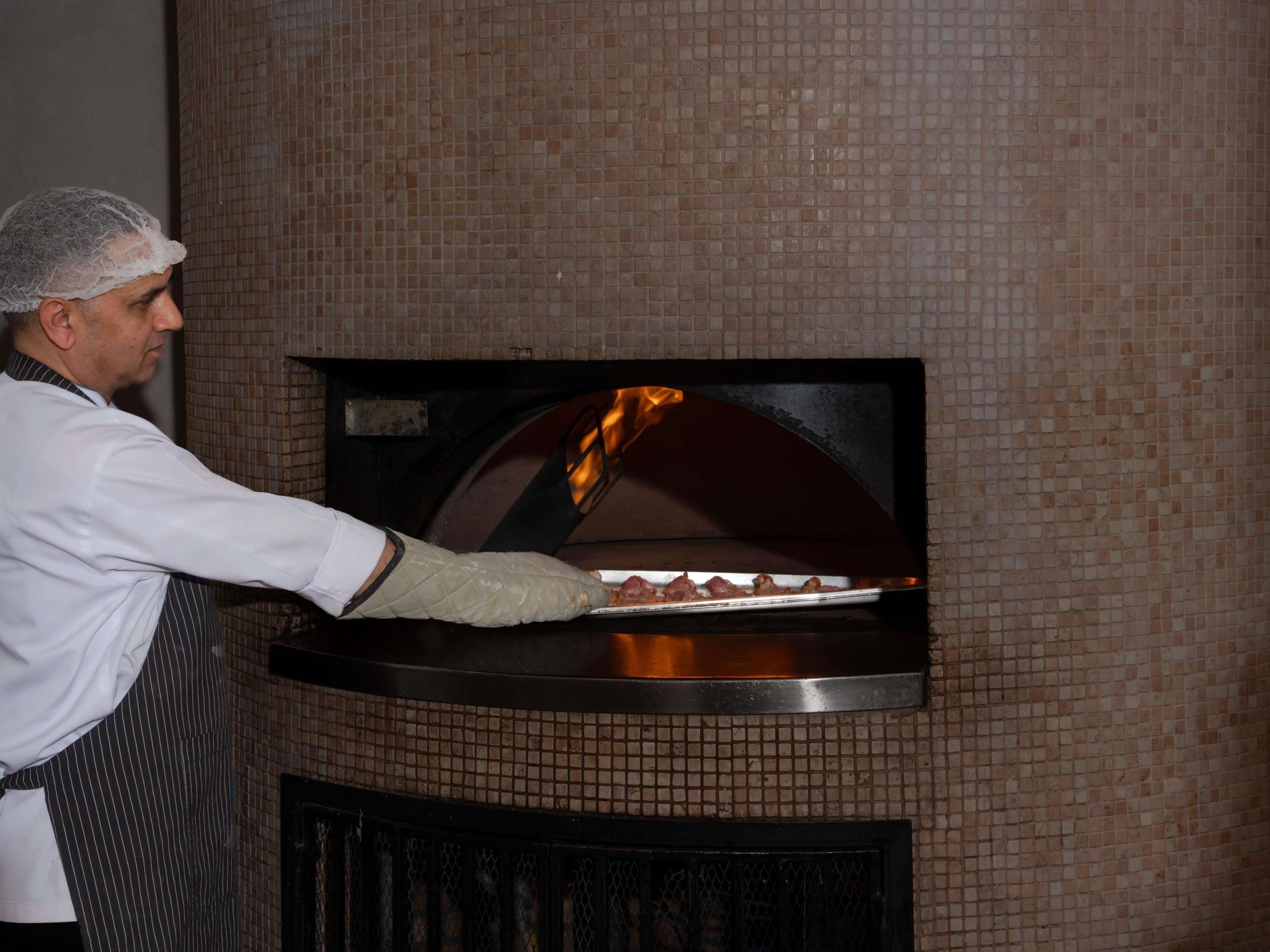 A person in a white shirt and apron placing pizza into a brick oven.