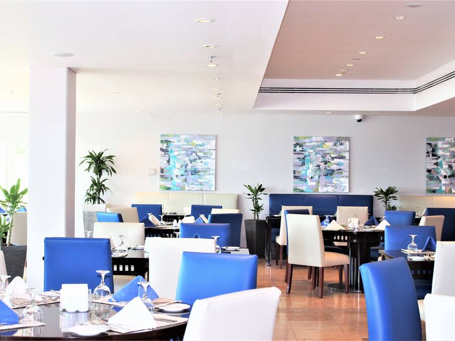 A modern restaurant with blue and white chairs, tables set for dining, and abstract art on the walls.