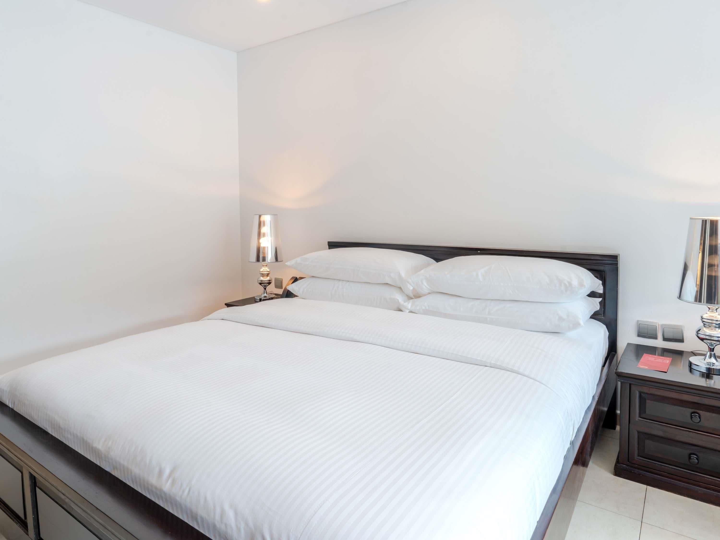 A hotel room with a large bed, a bedside table with a lamp, a nightstand with a phone, and a small drawer.