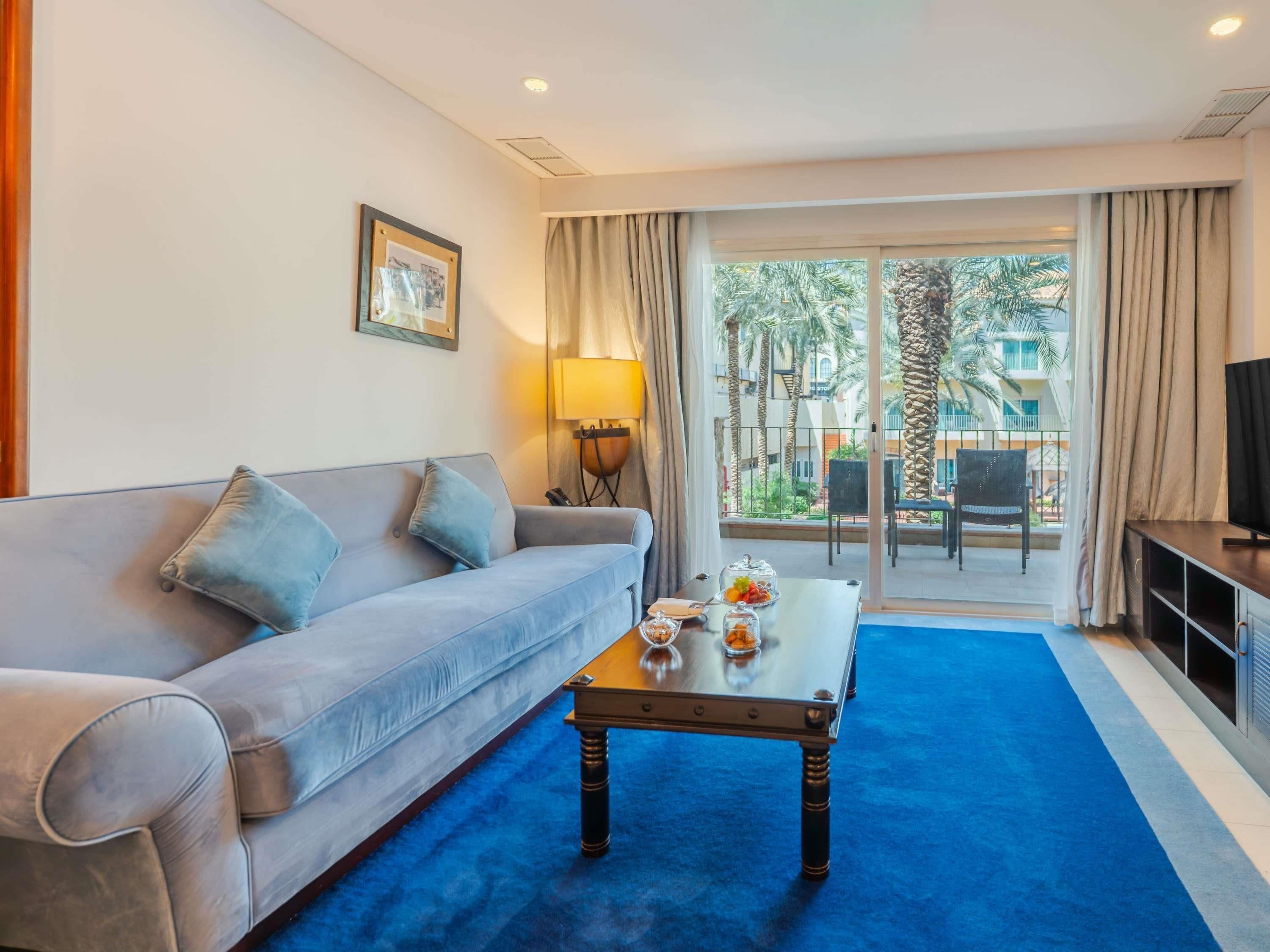 Une chambre d’hôtel avec un canapé, une table basse, une télévision et un balcon aménagé avec du mobilier d’extérieur.