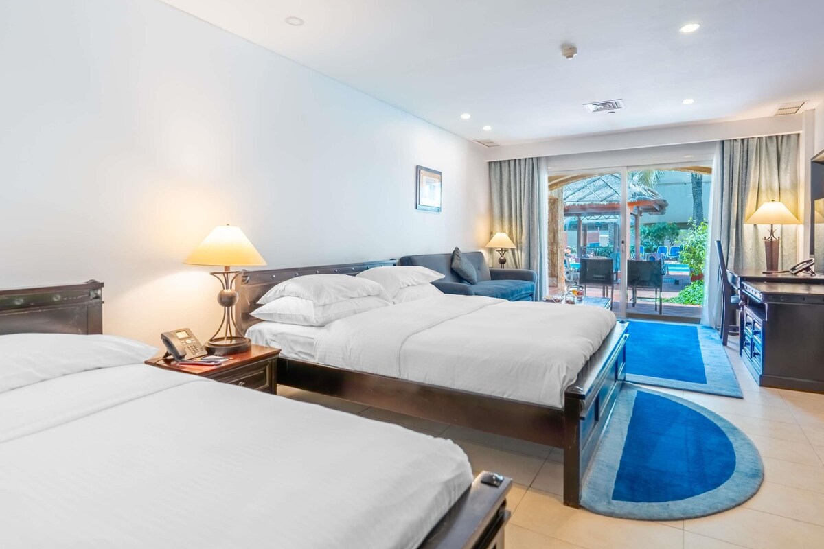Habitación de hotel con dos camas, un escritorio y vistas al área exterior.