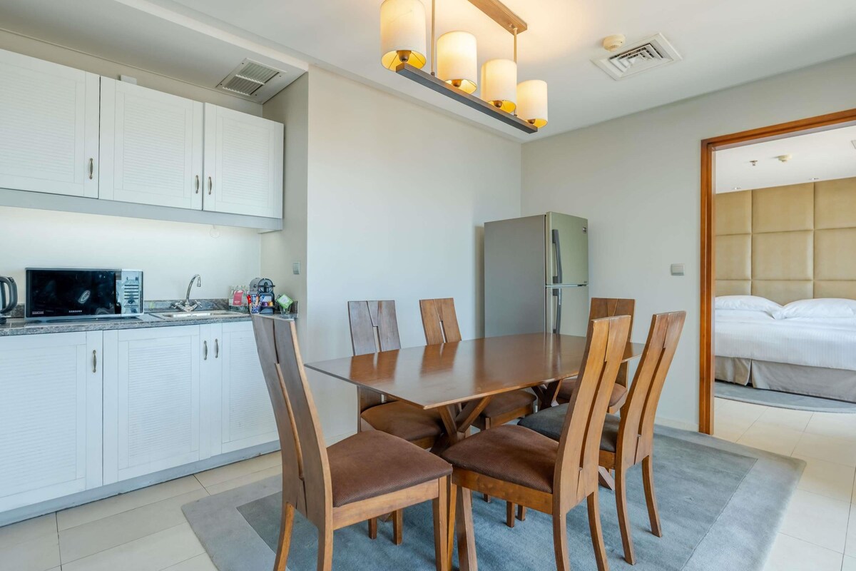 Una cocina moderna con armarios blancos, una mesa de comedor con sillas de madera, un refrigerador empotrado y una lámpara en el techo.