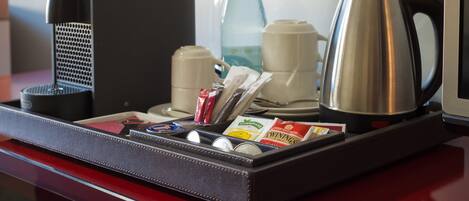 A tray with a coffee maker, a bottle, a kettle, and some coffee packets.