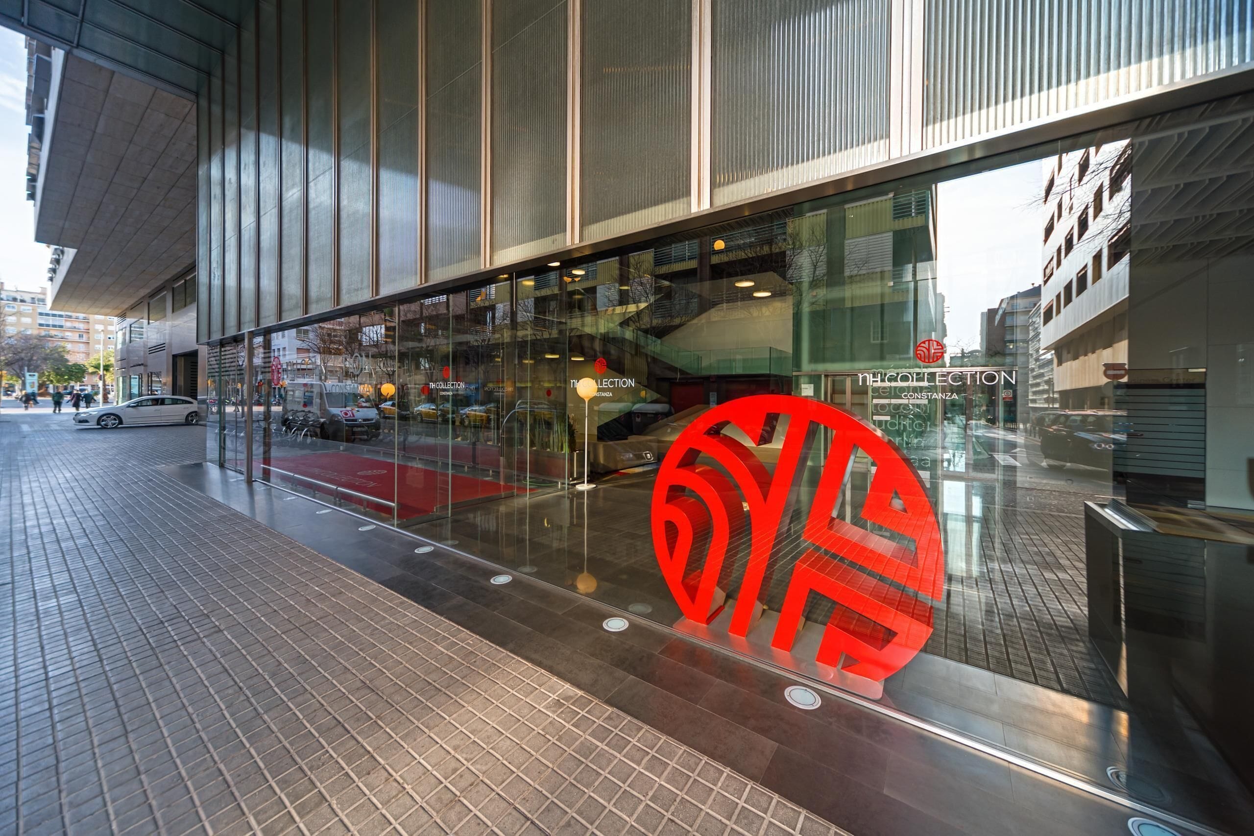 Un edificio moderno con grandes ventanales y un llamativo diseño circular rojo en la fachada.