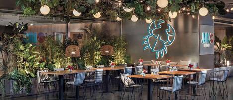 A restaurant with tables and chairs, surrounded by lush greenery and hanging lights.