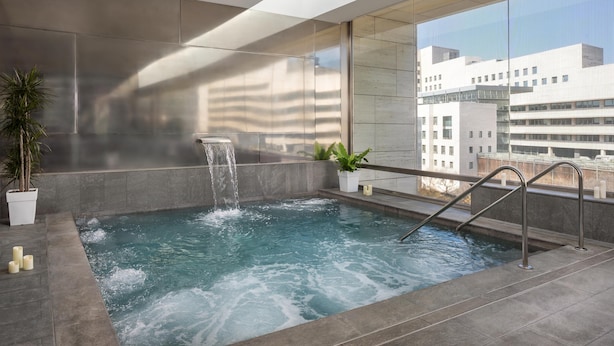 Piscina interior moderna con una cascada, rodeada de grandes ventanales con vistas a la ciudad.