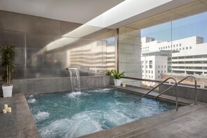 Piscina interior moderna con una cascada, rodeada de grandes ventanales con vistas a la ciudad.