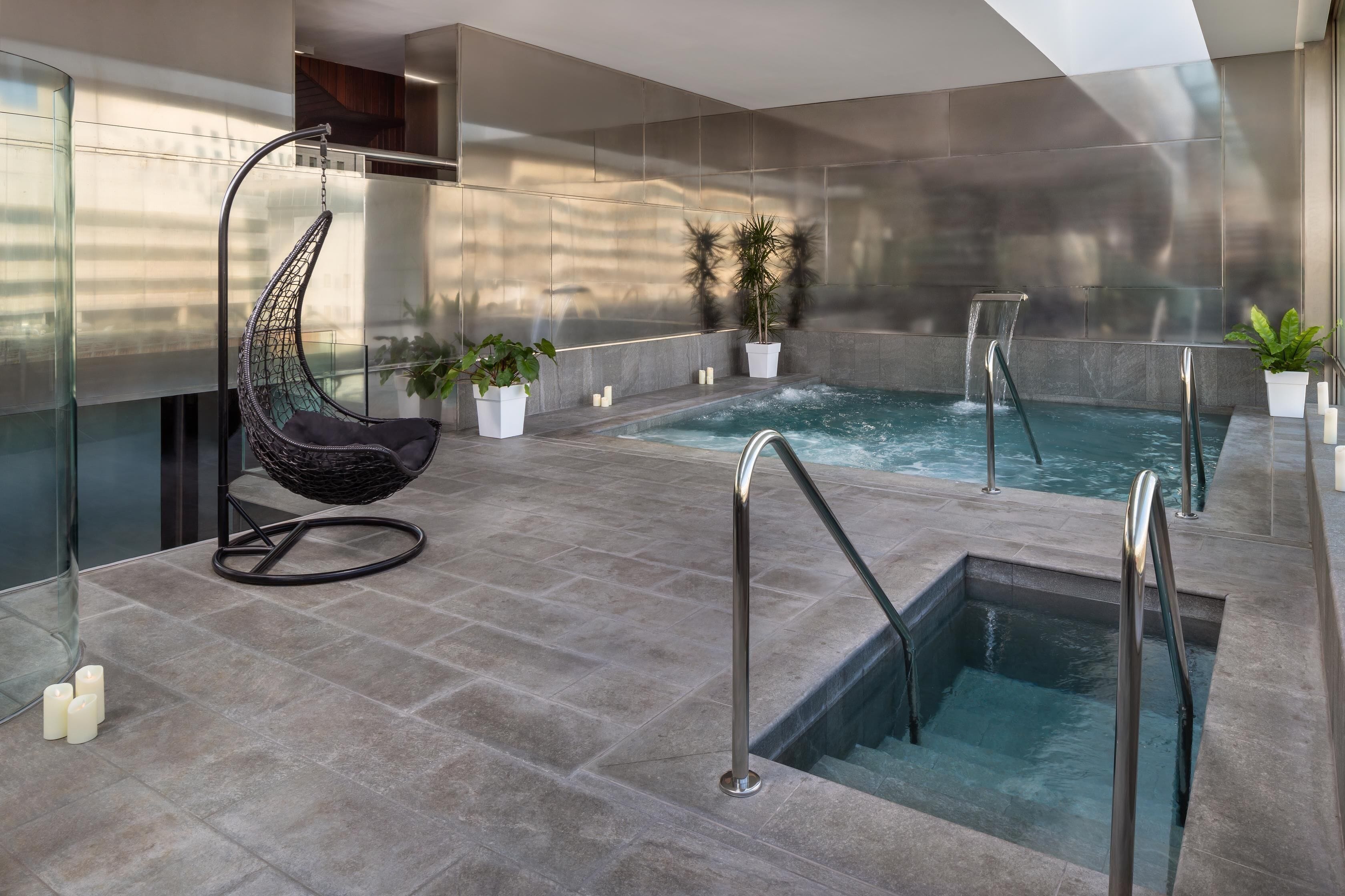 Un área interior de piscina moderna con una silla colgante, un jacuzzi pequeño y plantas en macetas.