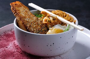 A bowl of food with noodles, a piece of fried fish, and a dumpling.