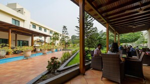 A covered outdoor seating area with wicker furniture, a pool, and potted plants. - Fiesta Royale Hotel (Accra)