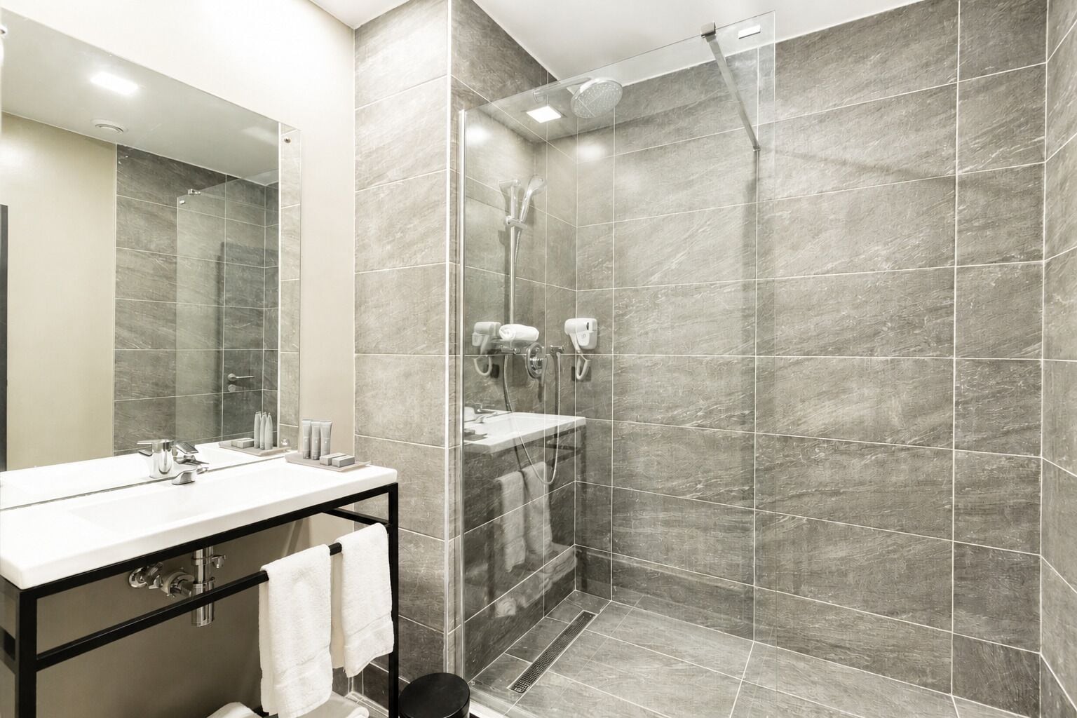 Un baño moderno con ducha de vidrio, tocador con espejo y barra para toallas.