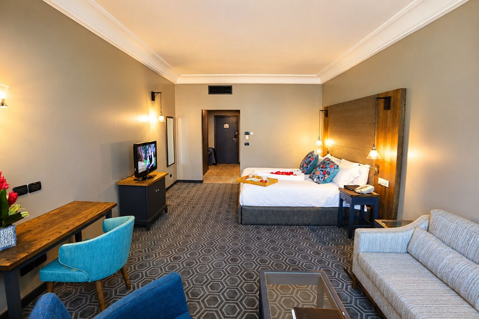 A hotel room with a bed, a desk, a chair, a sofa, and a television.