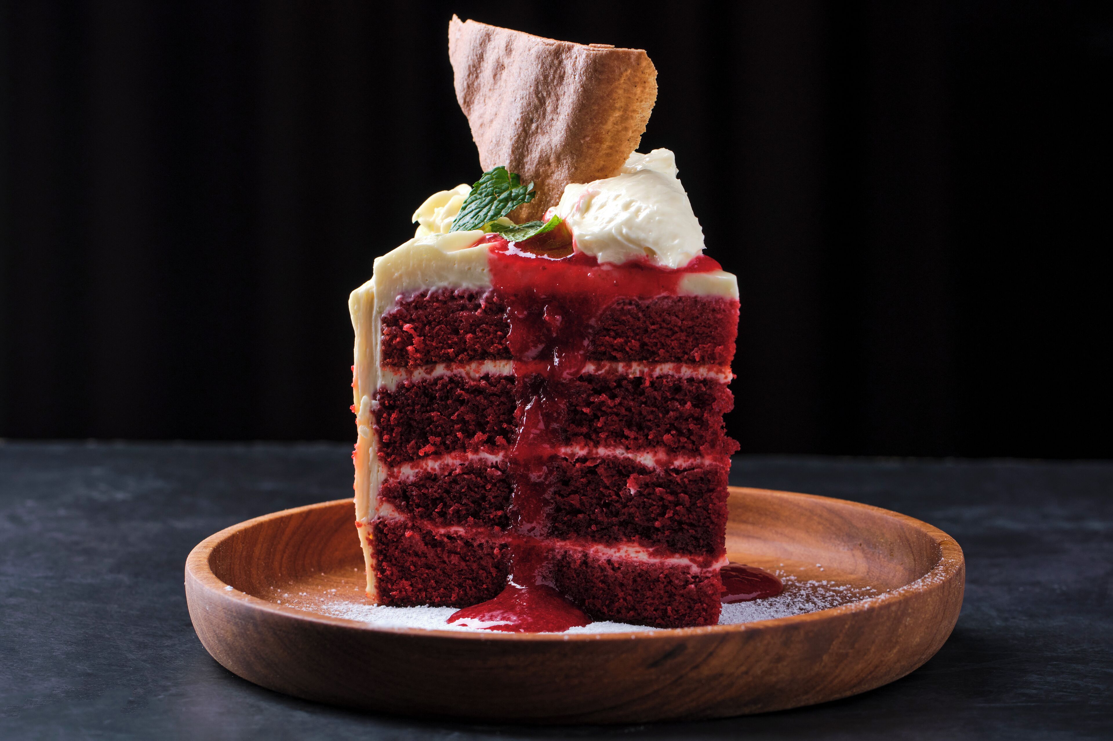 A slice of red velvet cake with cream and berries on a wooden plate.