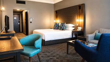A hotel room with a bed, two chairs, a desk, and a television.