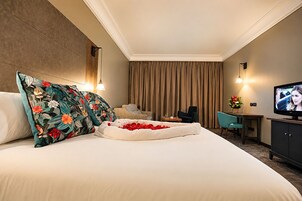 A hotel room with a large bed, a desk, a television, and a seating area.