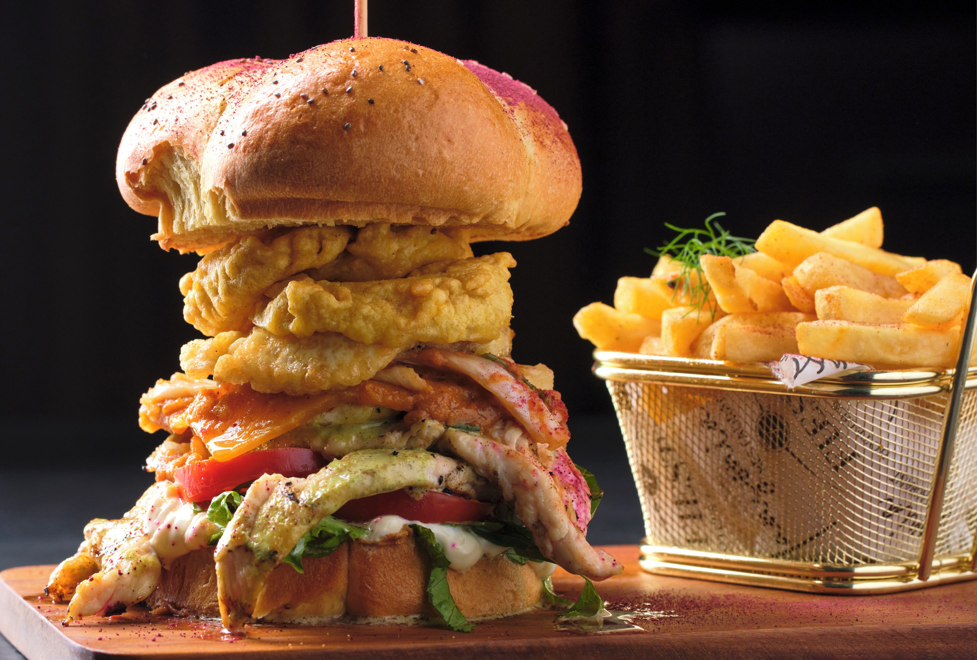 A large burger with fries on a wooden board.