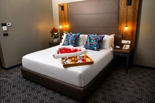 Habitación de hotel con una cama grande, una mesita de noche con teléfono y lámpara, y una bandeja con artículos para el desayuno.