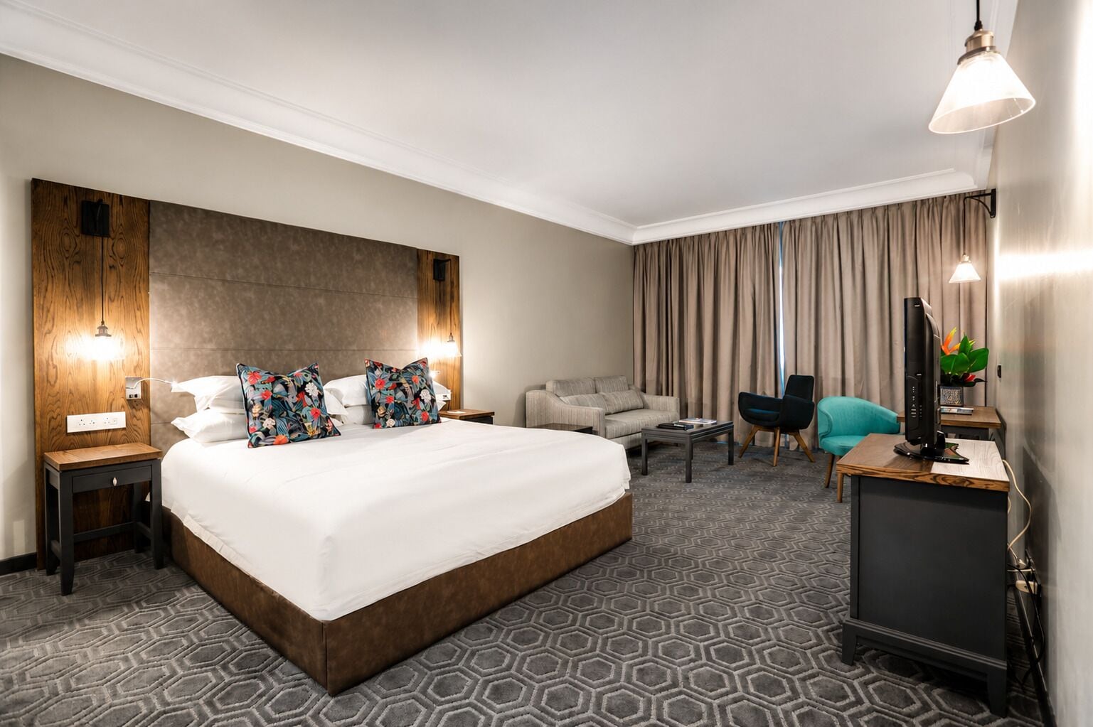 A hotel room with a large bed, a desk with a computer, a chair, a sofa, and a TV.