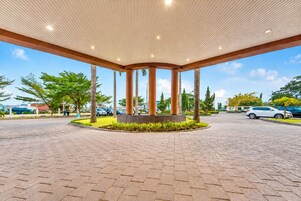 A covered outdoor area with a tiled floor, palm trees, and a central column structure.
