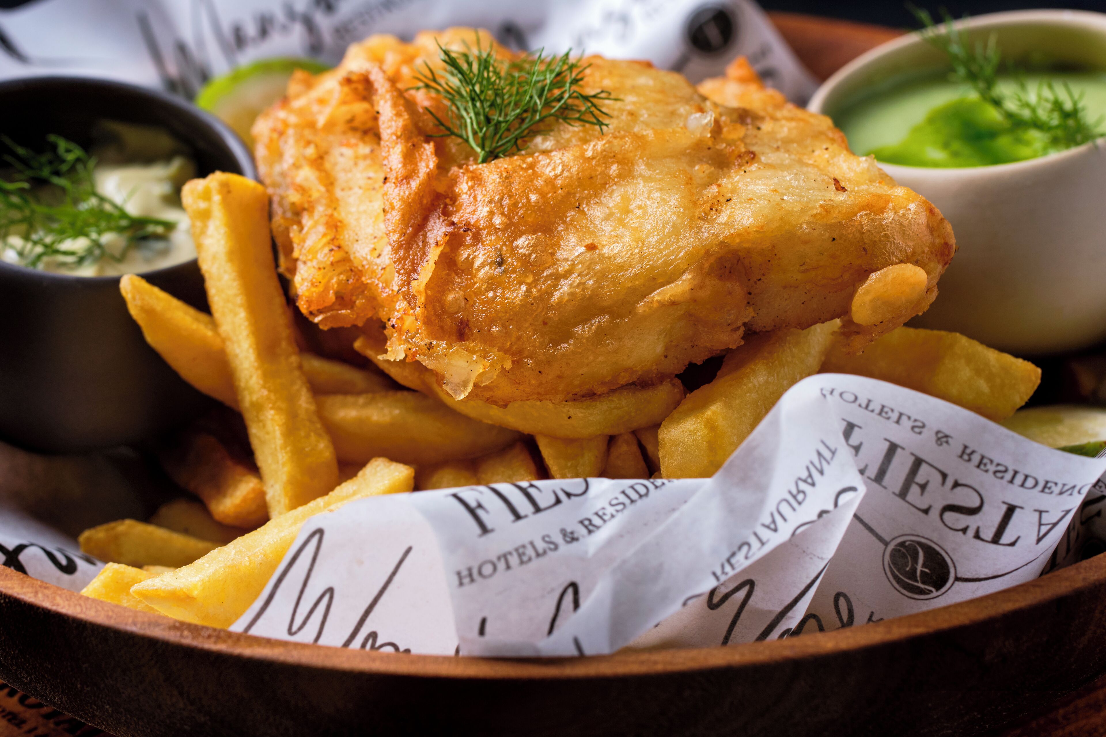 En træbakke med et fiskefilet, pommes frites og to dypsaucer.