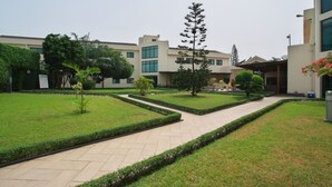 A courtyard with a paved walkway, neatly trimmed grass, and a variety of trees and shrubs. - Fiesta Royale Hotel (Accra)