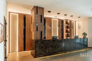Una zona de recepción moderna con mostrador de mármol, paneles de madera e iluminación colgante.