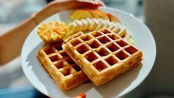 A person holding a plate with waffles and a fruit topping.
