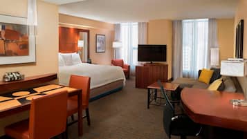 Una habitación de hotel con cama, escritorio, sofá, televisión y zona de comedor.
