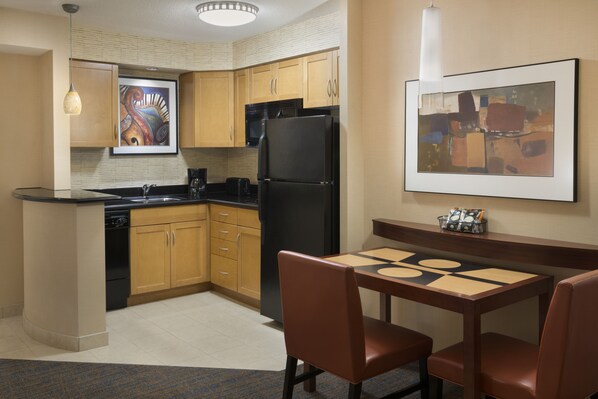 Una cocina compacta con armarios de madera, un refrigerador negro, una mesa de comedor con sillas y obras de arte en las paredes.