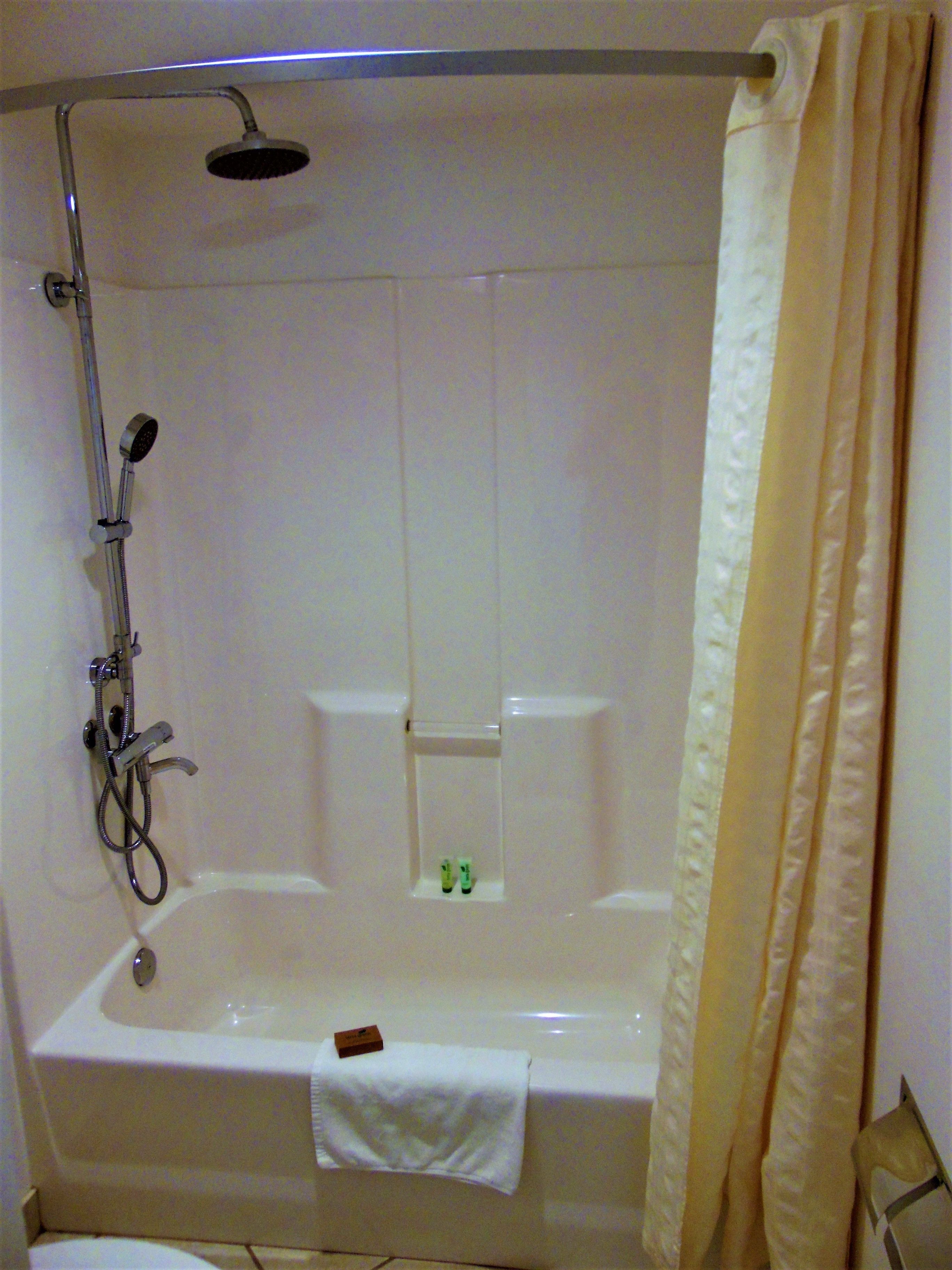 A shower with a handheld showerhead, a handheld shower attachment, and a towel rack with a towel.