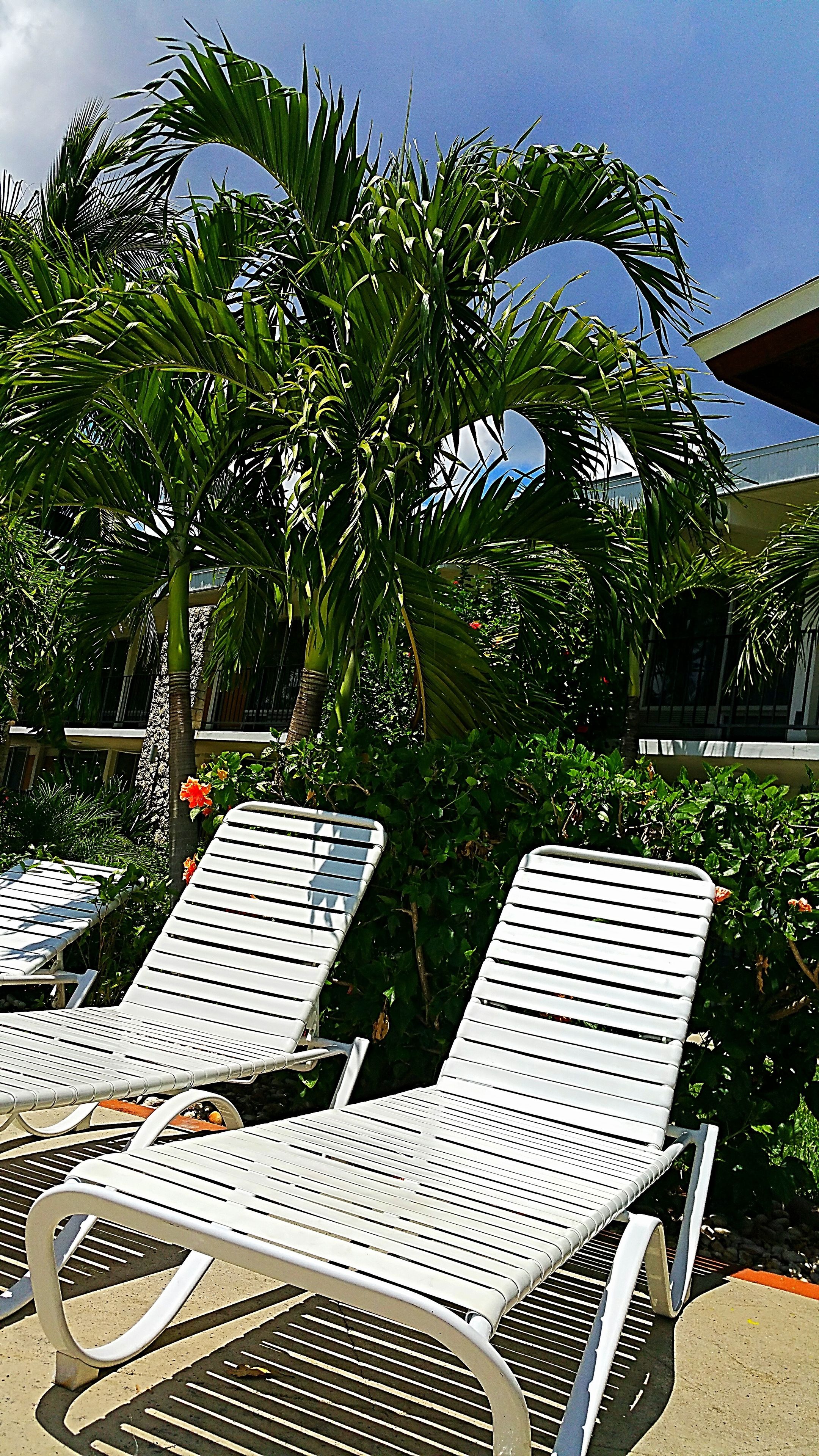 Two white lounge chairs with metal frames, positioned on a concrete surface with a metal grill pattern.