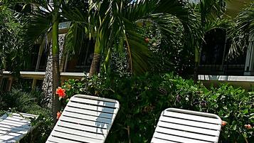 Deux fauteuils de relaxation blancs, dotés d’une structure en métal, sont placés sur une surface en béton ornée d’un motif en forme de grille métallique.