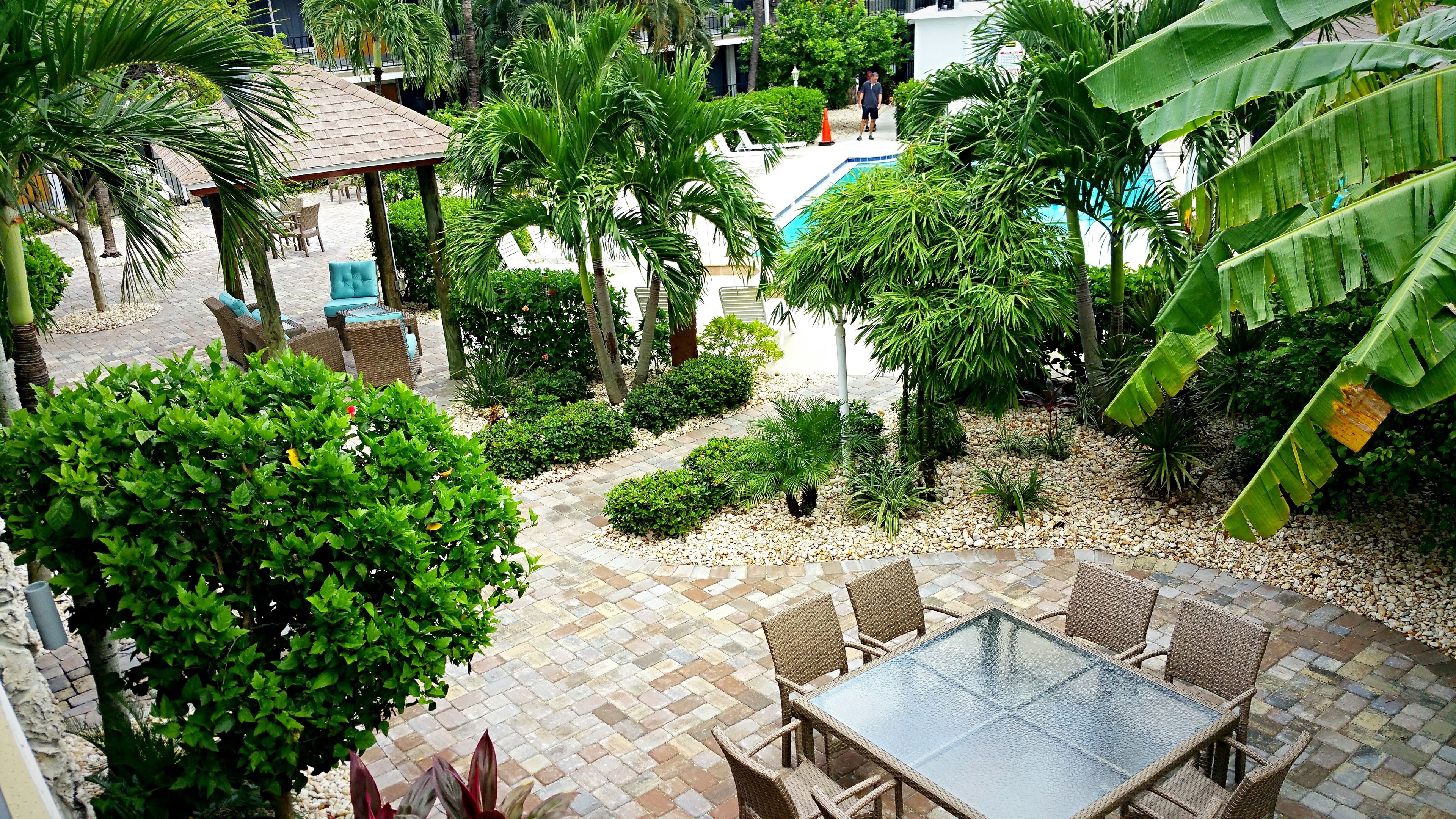 A patio area with wicker furniture, a pool, and lush greenery.