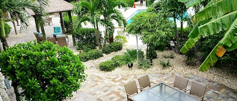A patio area with wicker furniture, a pool, and lush greenery.