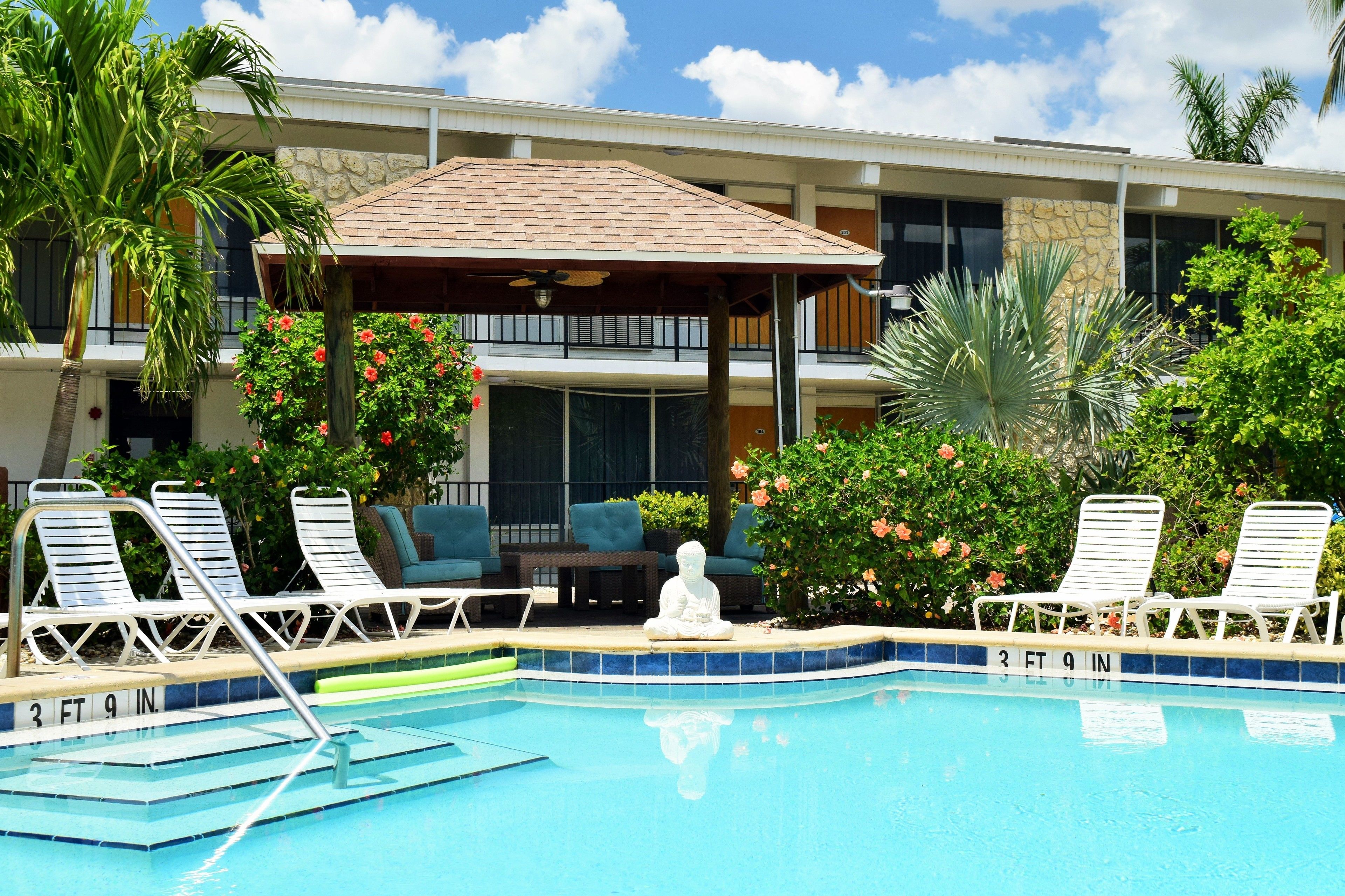 A pool area with lounge chairs, a Buddha statue, and a covered seating area.