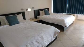 Two single beds with white linens, a nightstand, and a window with curtains.